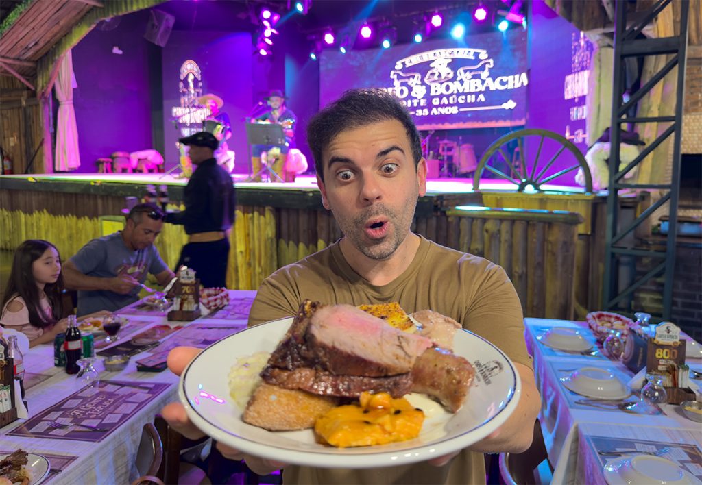 Garfo e Bombacha churrascaria: 5% de desconto no site oficial 2 Francisco do Aventurando Tchê segurando um prato cheio de churrasco na frente do palco da churrascaria Garfo e Bombacha em Canela
