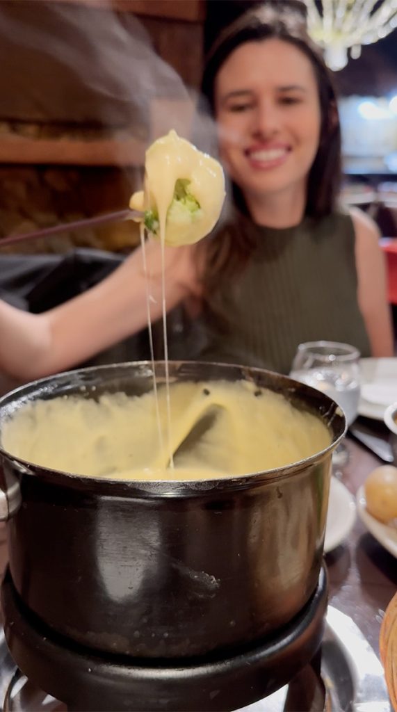 Alessandra do Aventurando Tchê mergulhando o brócolis no fondue de queijo no restaurante La Famille de Gazon