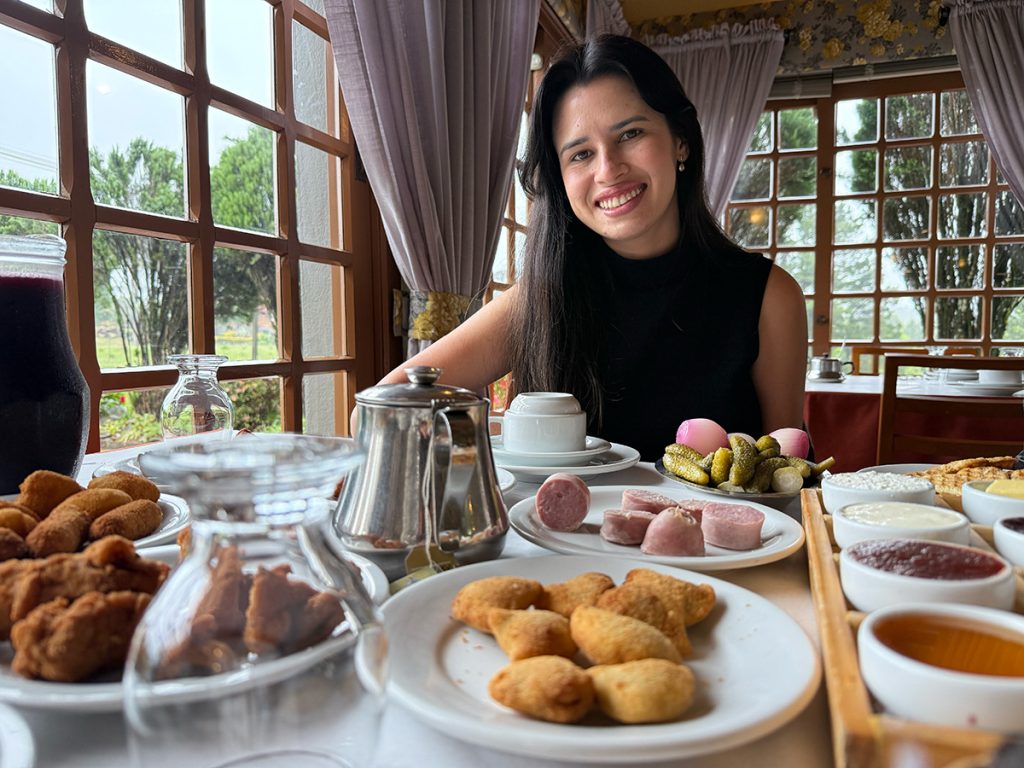 Gramado Café Colonial: 10% de desconto no site oficial 5 Alessandra do Aventurando Tchês sorrindo com a mesa cheia de comida no Gramado Café Colonial